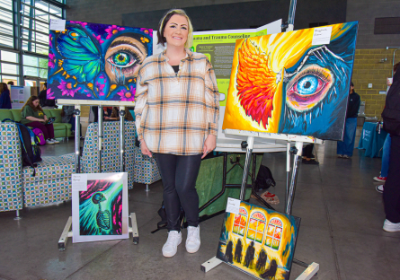 CGCC student poses with her original paintings at the Honors & HIPs Showcase