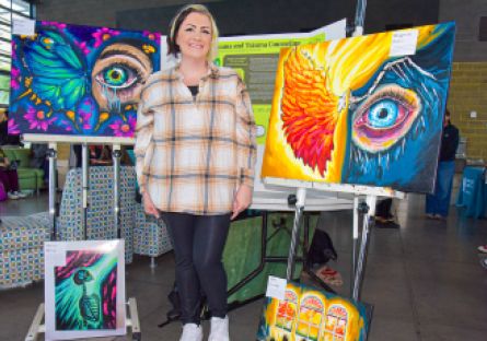 CGCC student poses with her original paintings at the Honors & HIPs Showcase