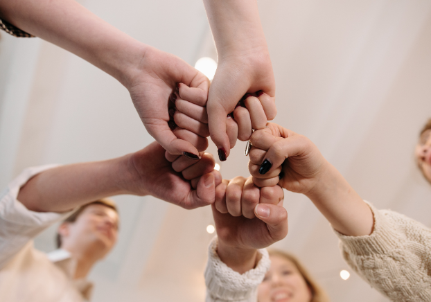 Several people join hands in a circle, symbolizing teamwork, unity, and support.